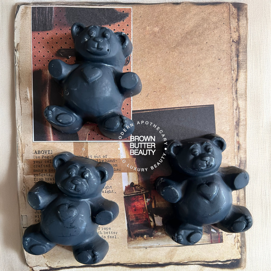 Three black Teddy bear-shaped soap bars on a textured surface with 'Brown Butter Beauty' branding.